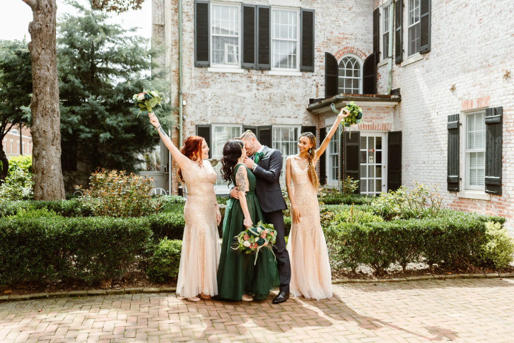 Bride and groom kiss with their bridesmaids celebrating in front of an English-style manor during their Old Town Alexandria elopement. 