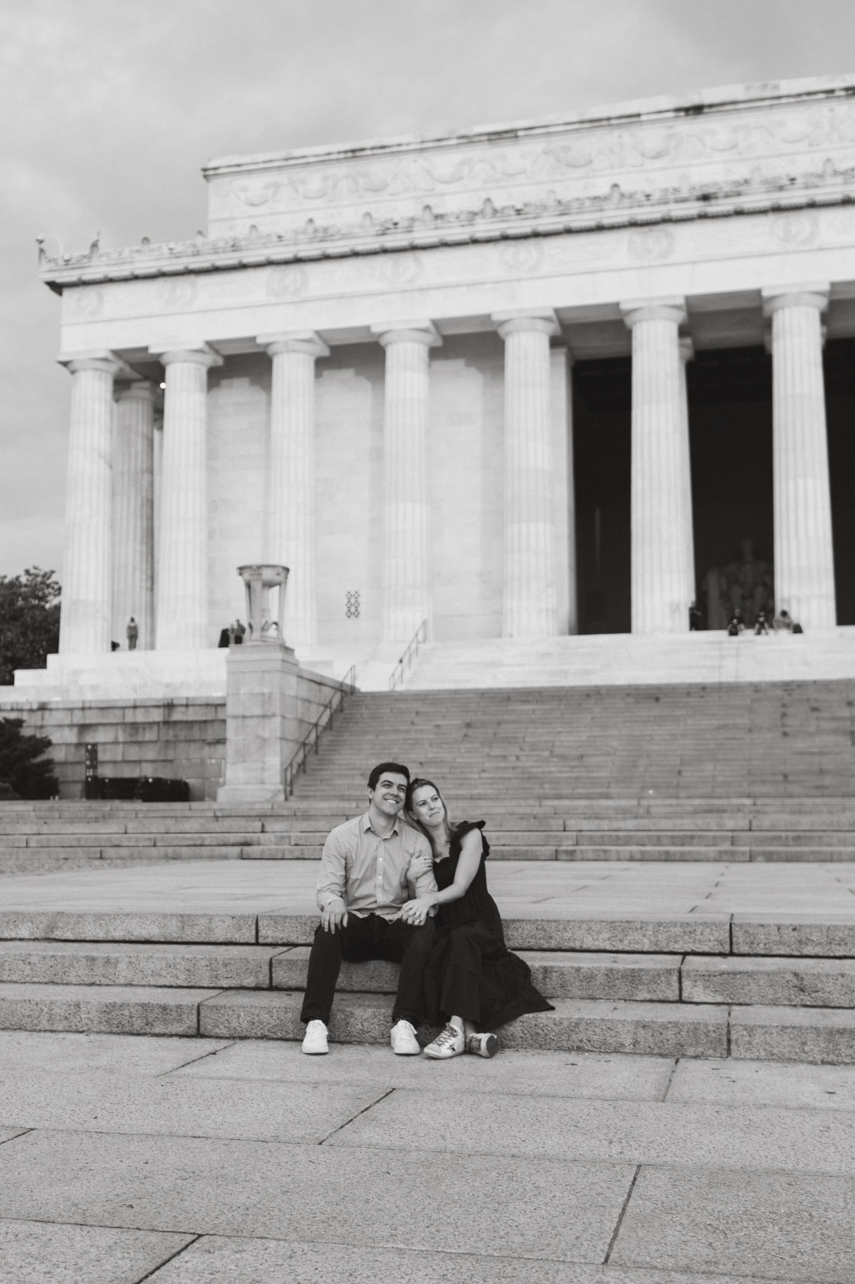 Black and white romantic photo of husband and wife sitting on the steps of the Lincoln Memorial during a sunrise photoshoot in DC. 