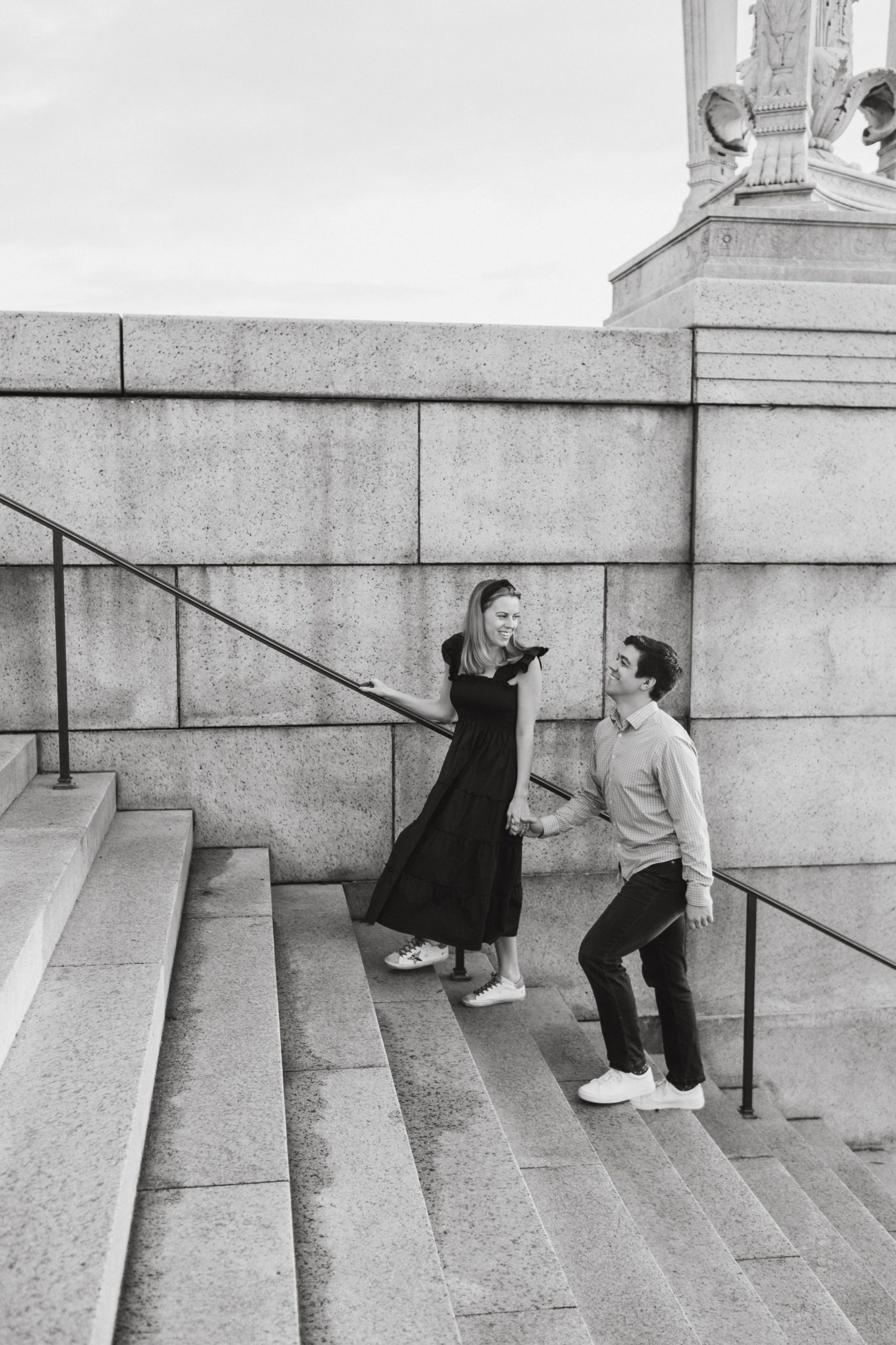Black and white photo of woman leading man up a set of stairs. 