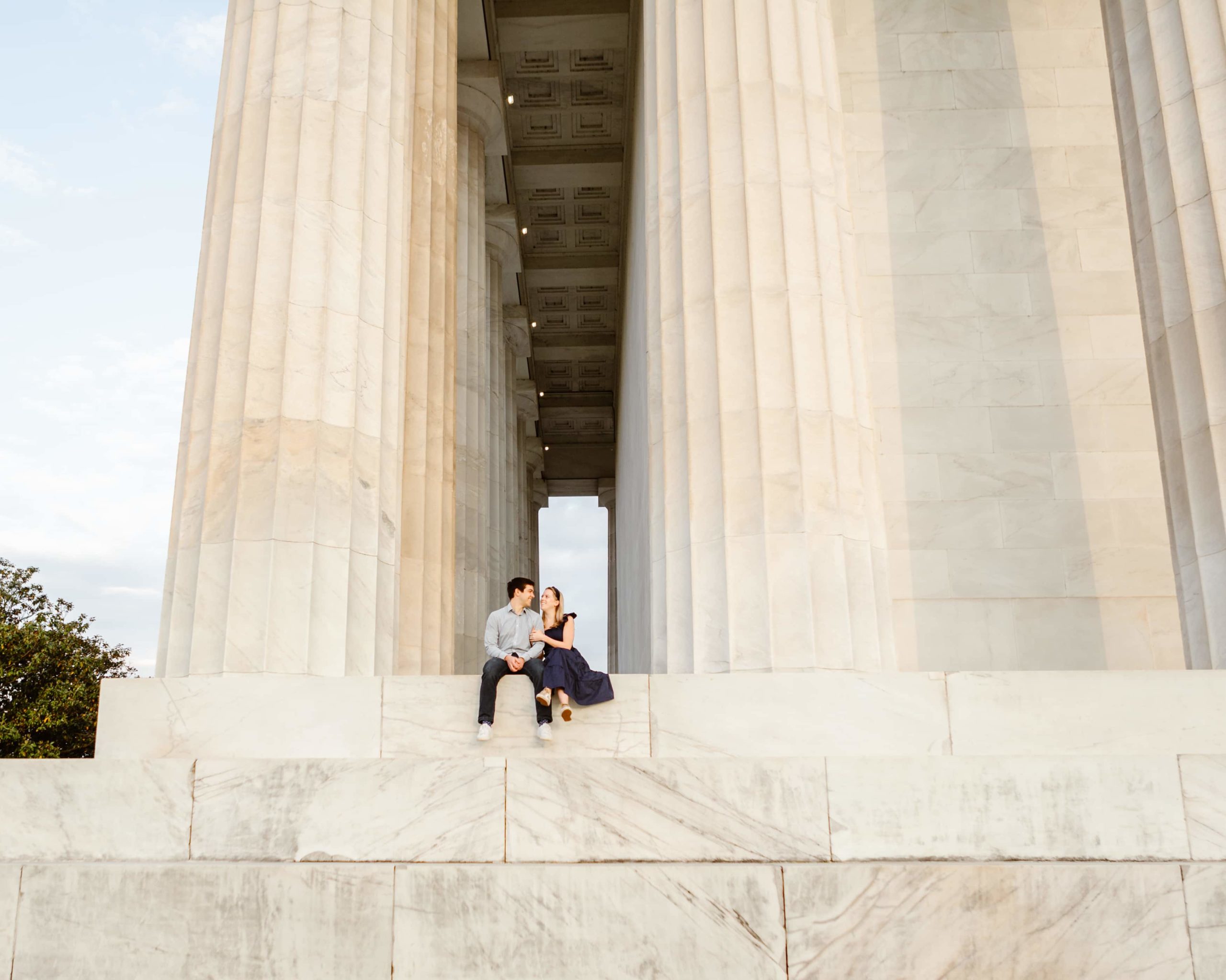 Couple sit together at the Lincoln Memorial watching the sunrise during DC engagement photos. 