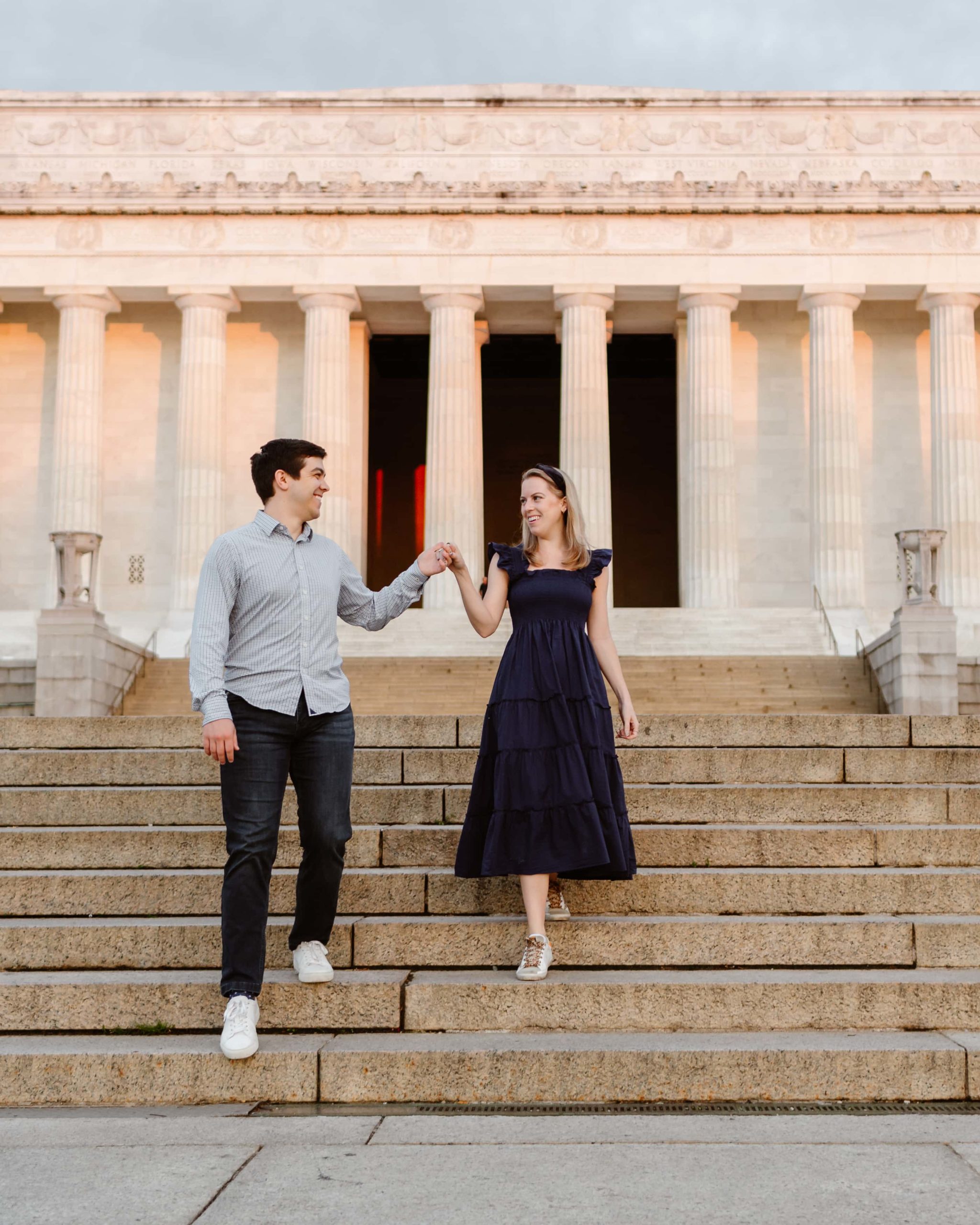 Couple walks down the Lincoln Memorial stairs at sunrise during engagement session.