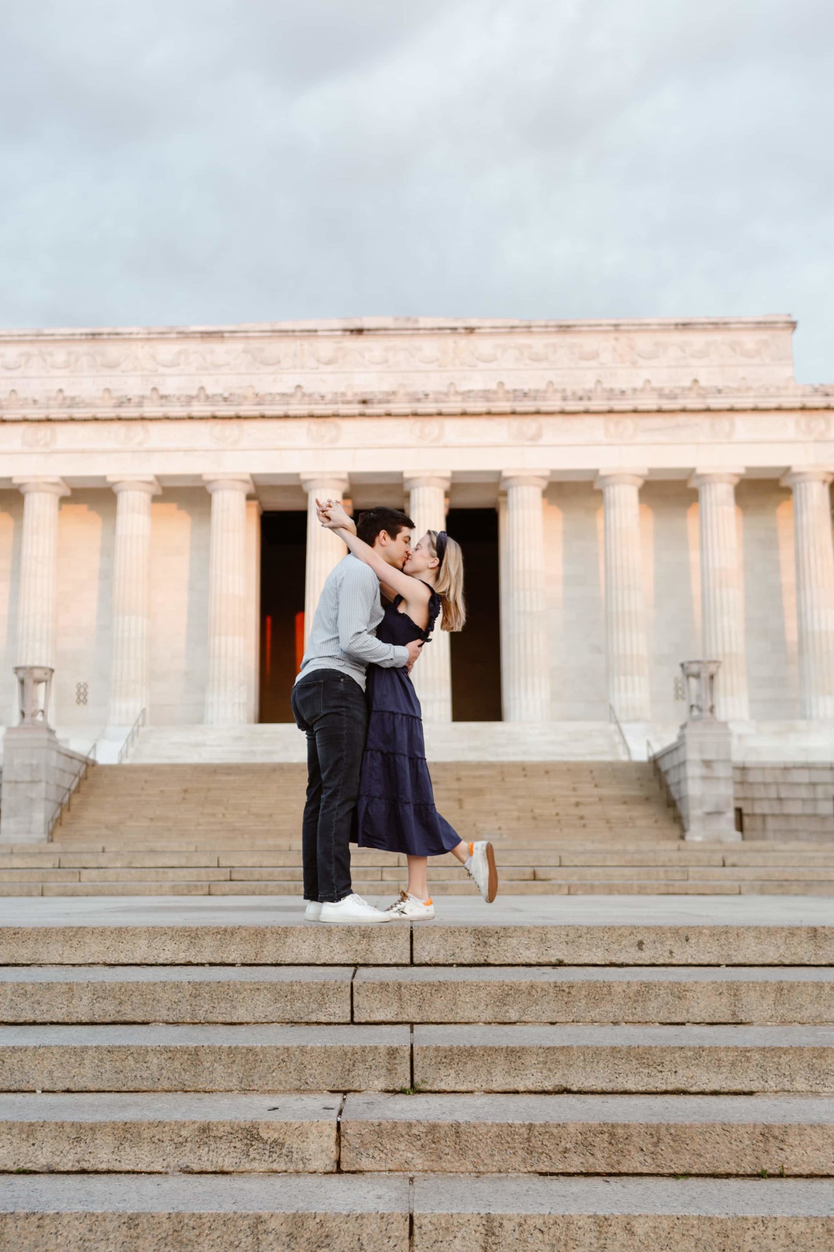 Couple embrace and kiss on the steps of the Lincoln Memorial at sunrise during their engagement session in Washington DC.