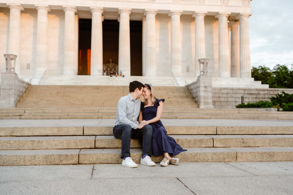 Couple sits on the Lincoln Memorial steps together with the sun shining on the columns and the Lincoln Statue in DC.