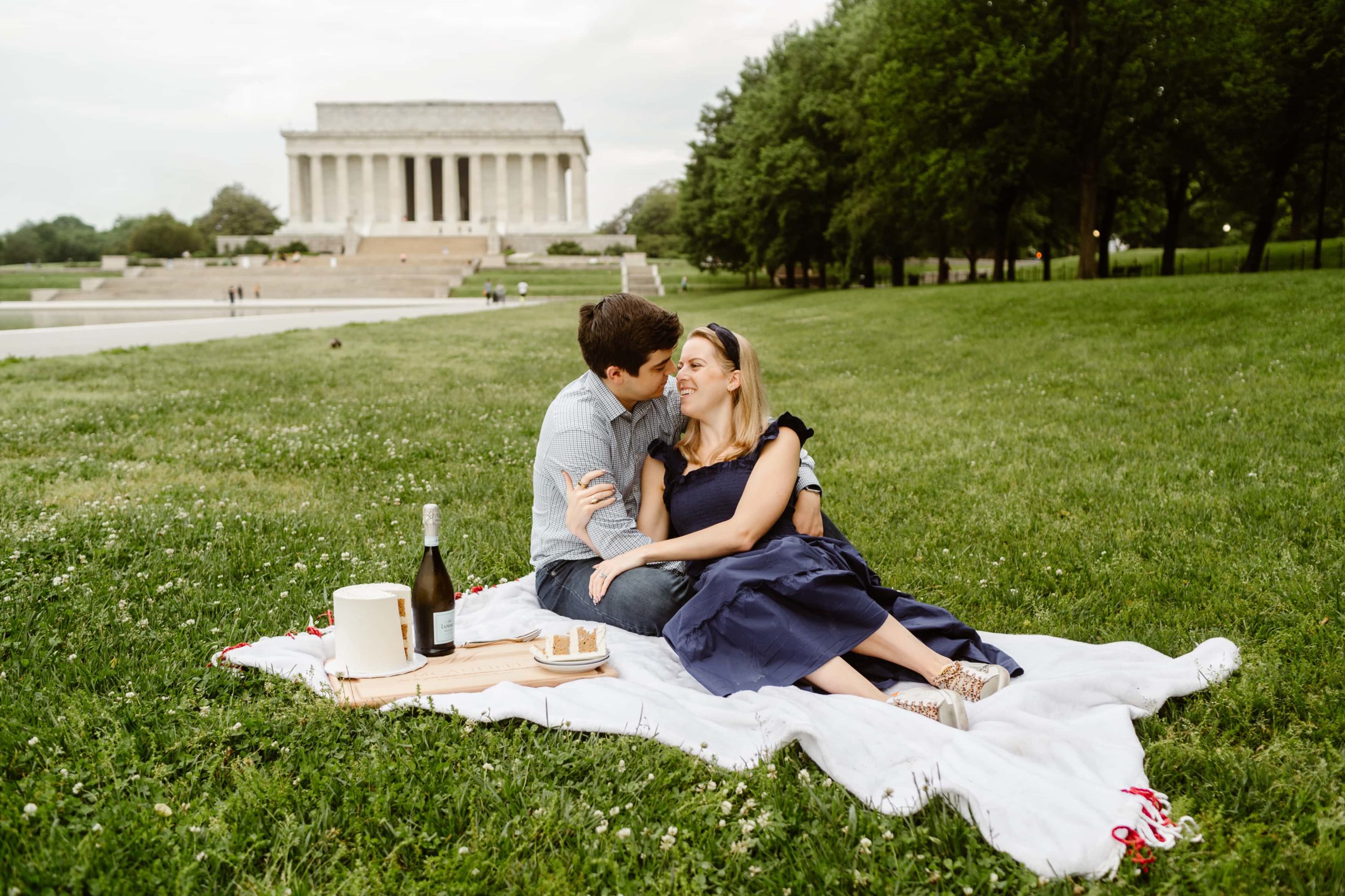 Couple lounges together in the grass on a blanket in front of the Lincoln Memorial during a DC engagement photoshoot. 