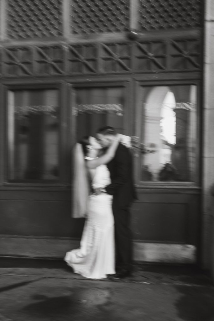 black and white blurry vintage photo of bride and groom kissing in front of Union Station building with her foot kicked up.