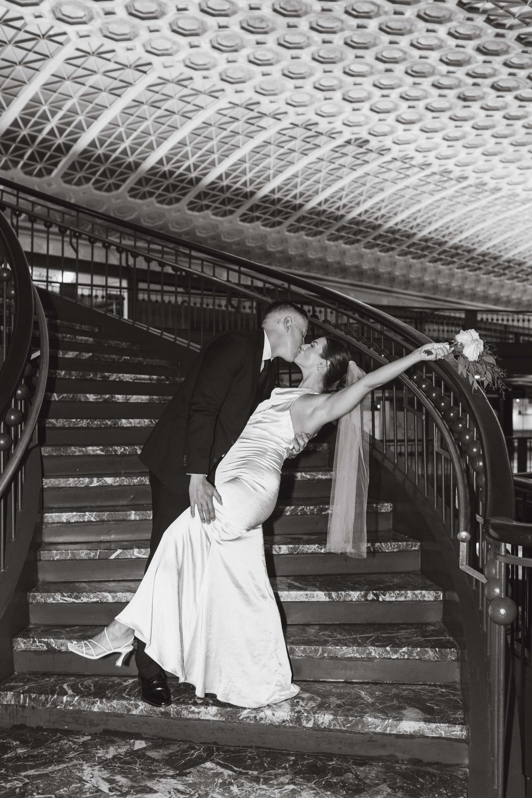 Bride and groom kiss on a staircase in Union Station, DC with bride's arm raised holding a bouquet.