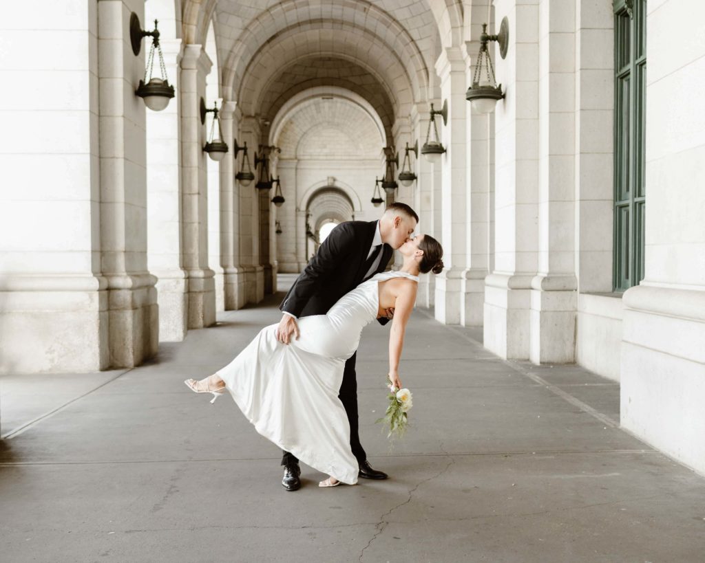 Bride and groom dip kiss holding a white flower bouquet under the arches at Union Station in Washington DC