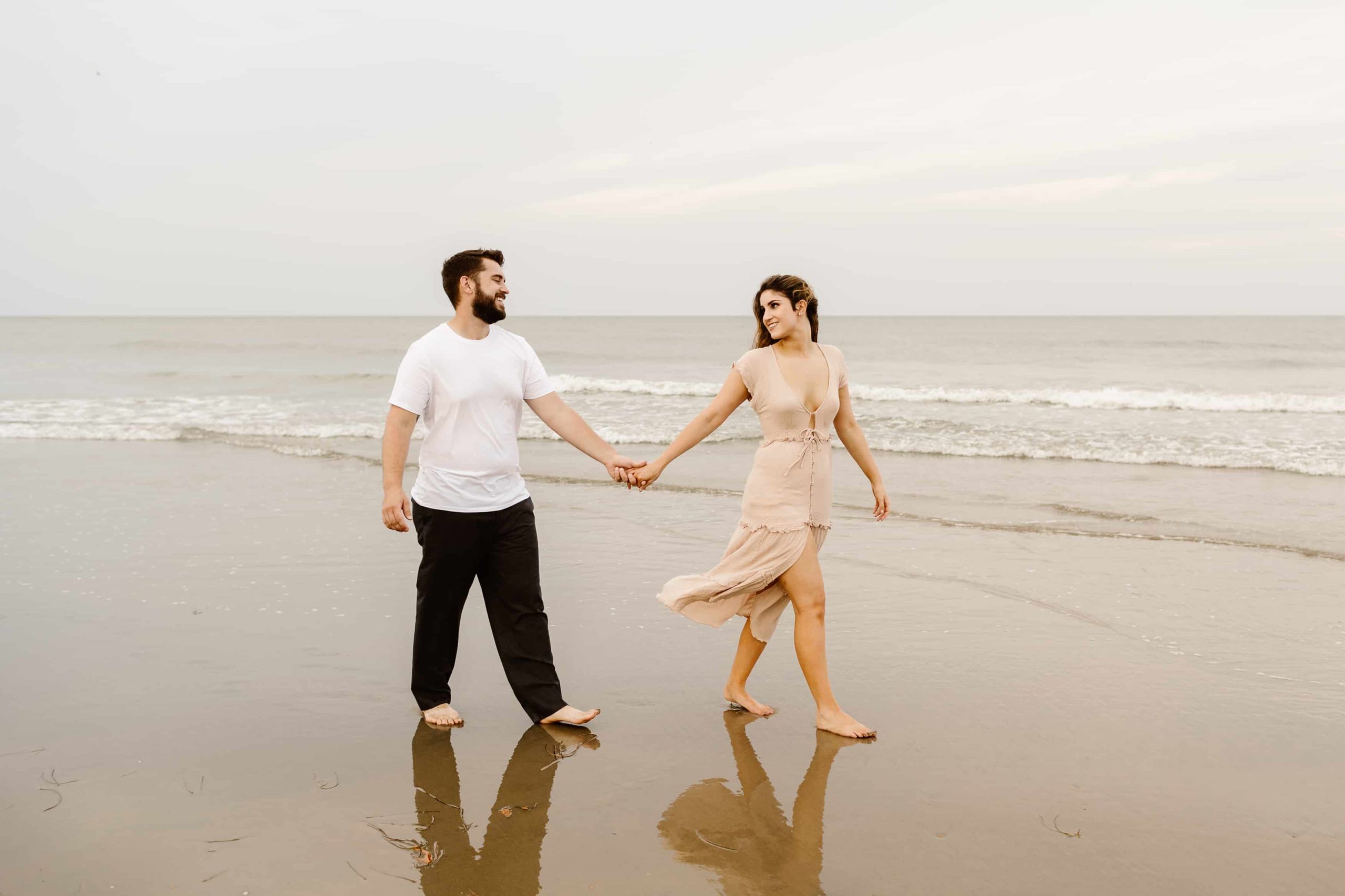 Couple walks in the sand holding hands along the ocean in Virginia Beach.