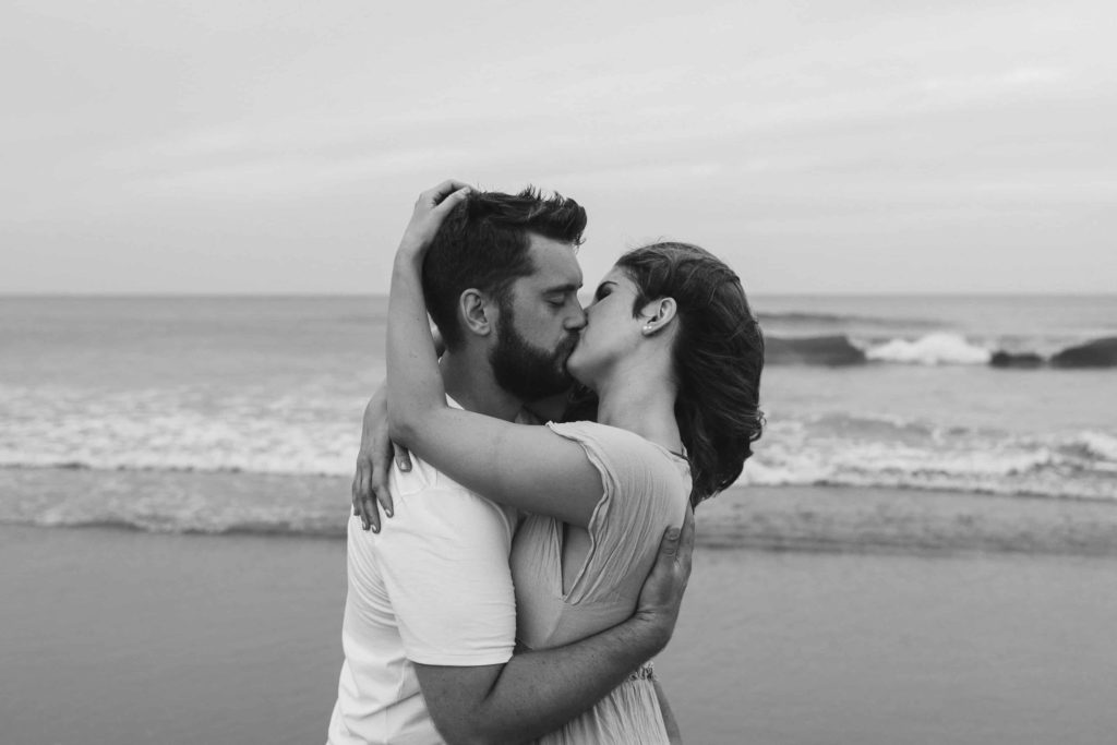 Black and white photo of couple kissing on the beach. 