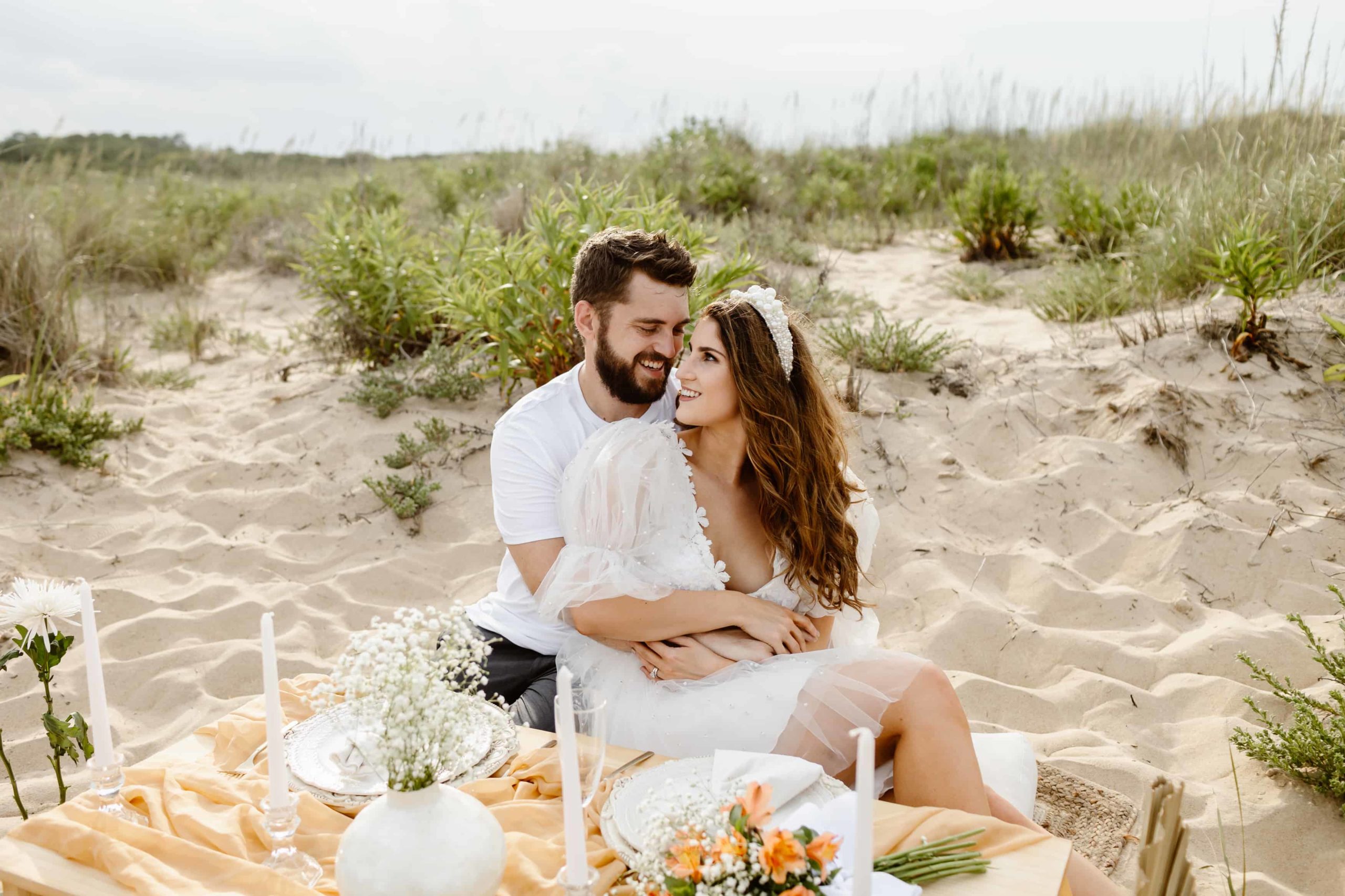 Bride and groom sitting a luxury picnic on in Virginia Beach as they celebrate their wedding in a short wedding dress.