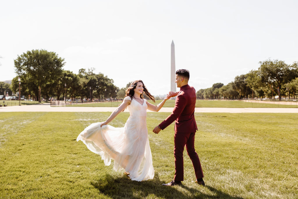 Groom spins bride who is holding her dress out on the National Mall in front of the Washington Monument.