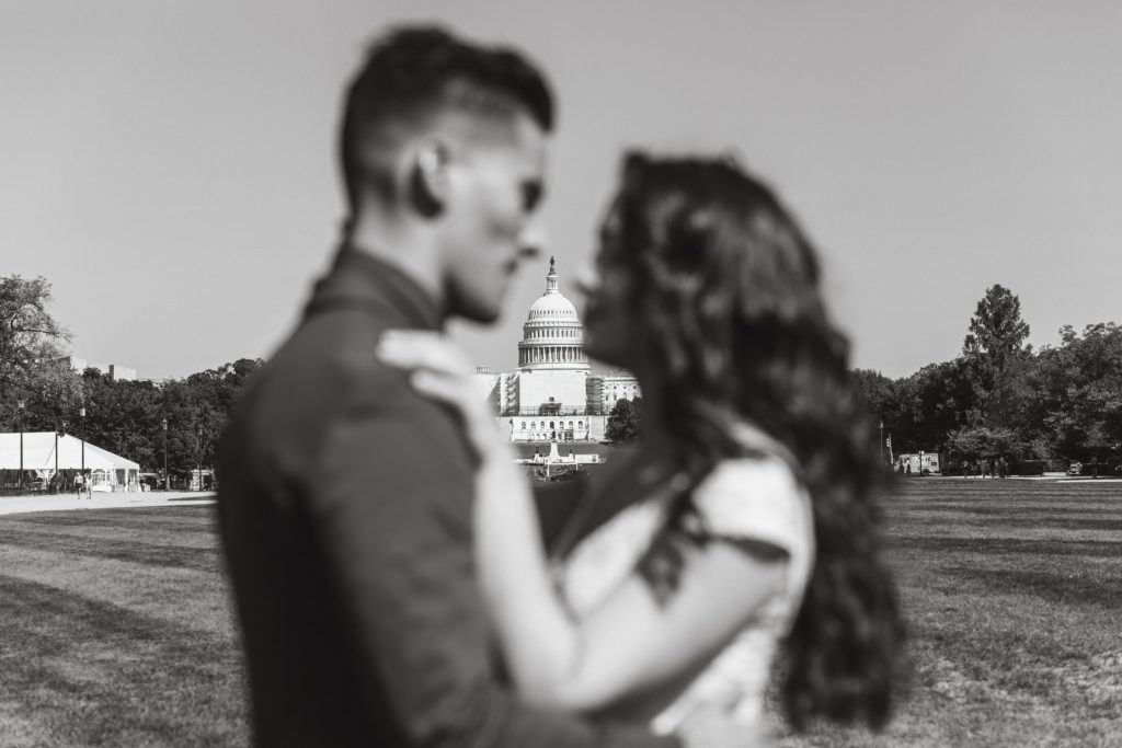 Black and white images of the US Capital Building is in focus with a bride and groom out of focus.