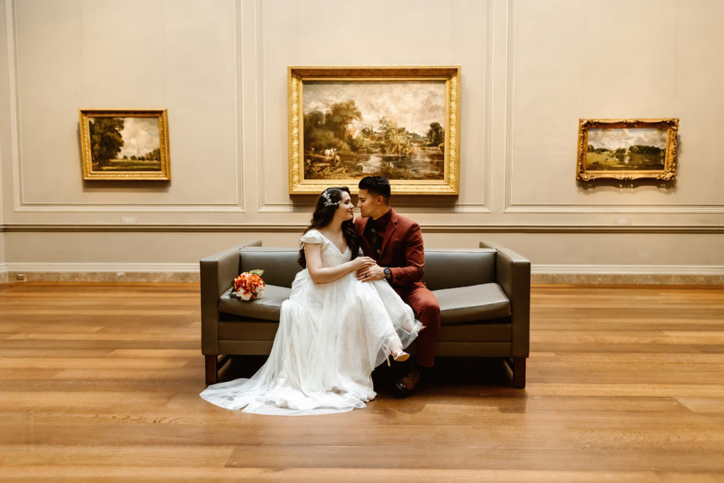Wedding couple sits on couch in front of art in the National Gallery of Art in Washington DC.