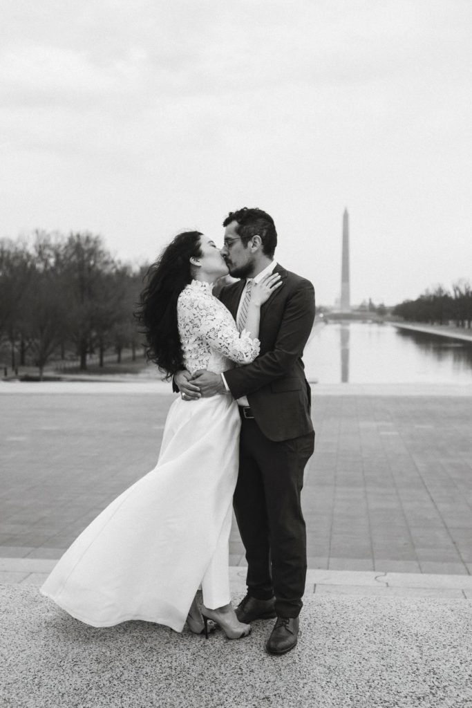 Black and white photo of bride and groom embracing and kissing in front of the Washington Monument in DC during their elopement day. 
