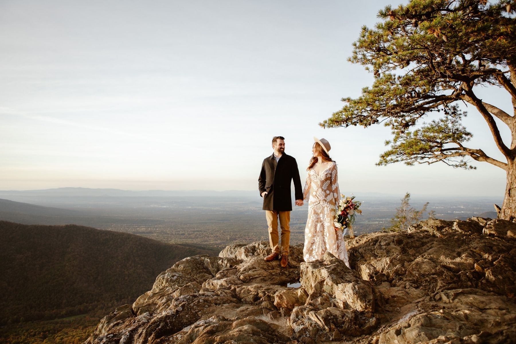 Bride in white dress holds hands with groom in Shenandoah National Park for a Virginia mountain elopement.