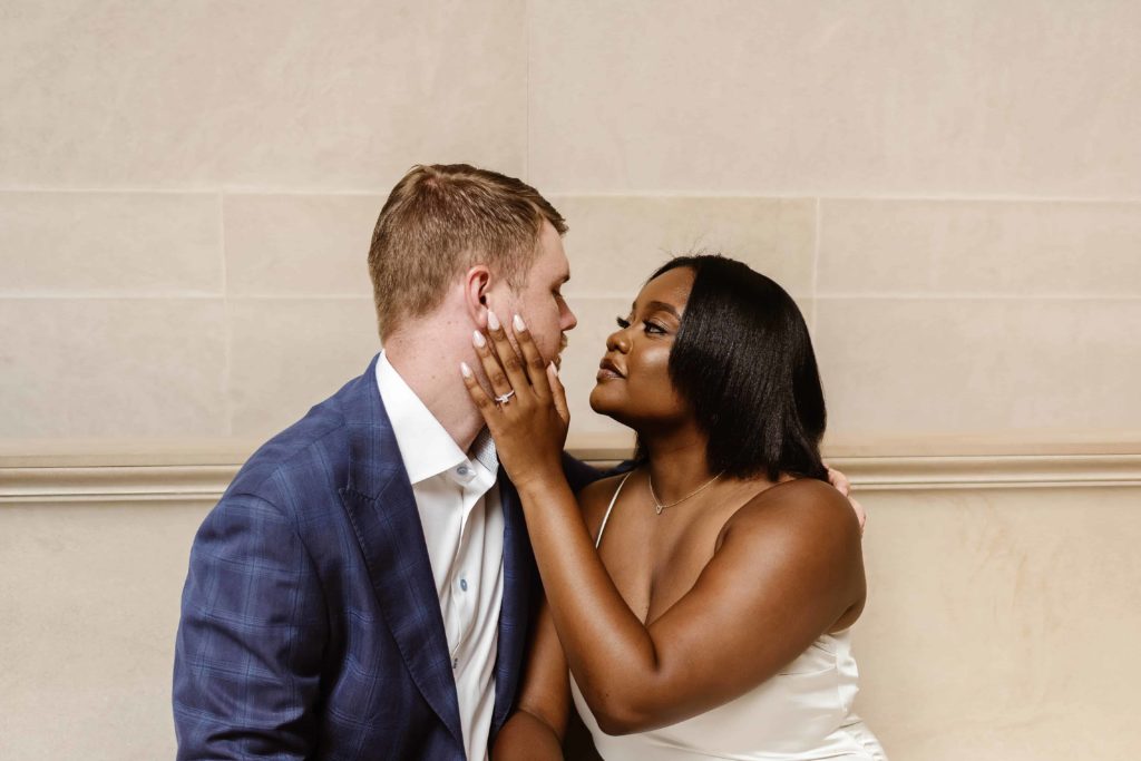 Woman hold man's face close to her while wearing an engagement ring in a DC art museum.