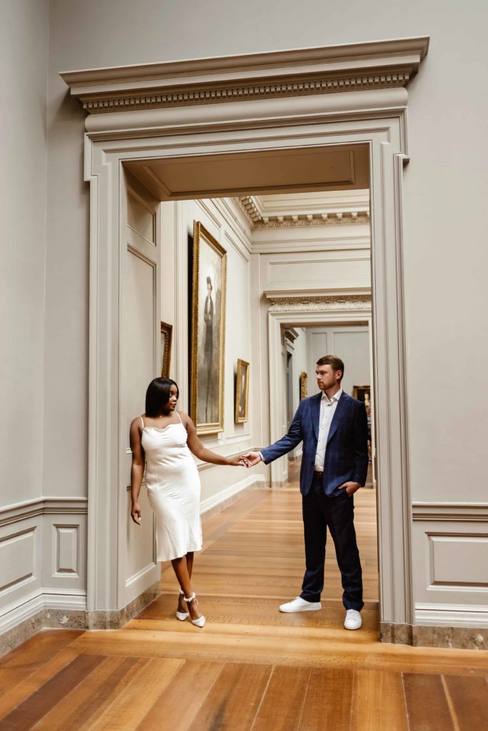 Man and woman hold hands in the archway in a DC art museum. 