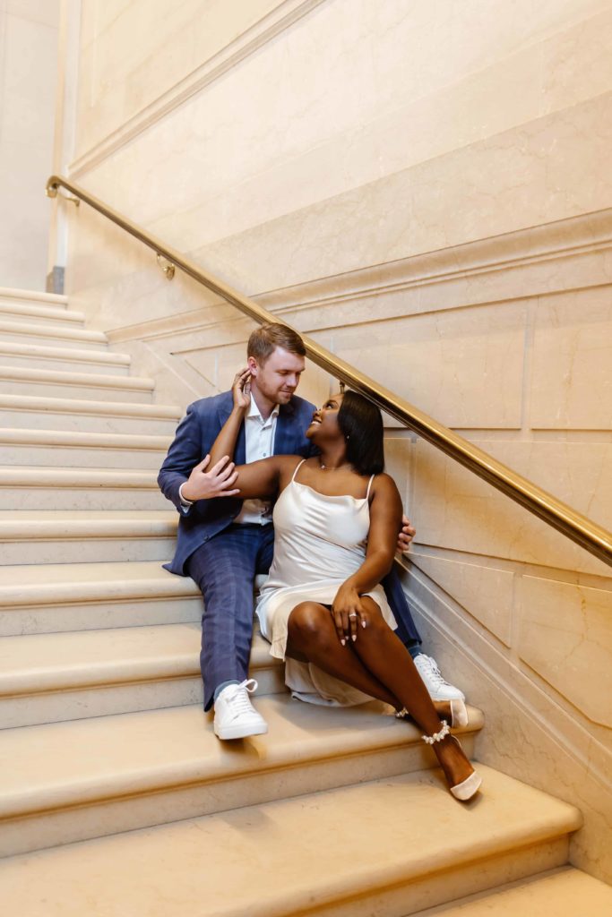 Bride and groom sit on white marble steps in an art museum in Washington DC.