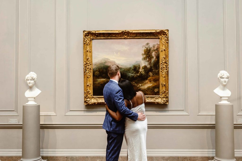 Couples stands arm in arm looking at a painting at the National Gallery of Art in DC. 