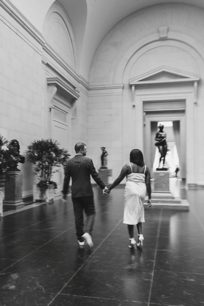 Black and white motion blur photo of bride and groom holding hands walking through an art museum in DC. 