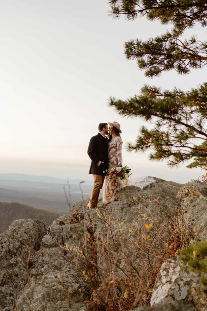 Bride and groom stand facing each other on a cliff in the Virginia mountains at sunset during their Raven's Roost Overlook Elopement. 