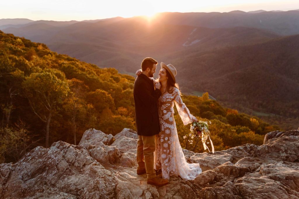A bride laughs and swings her arm back while hugging her groom as they both stand in the Virginia mountains at sunset during their Raven's Roost Overlook Elopement. 