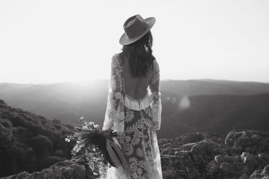 Black and white photos of a bride facing away from the camera during sunset in the mountains. 