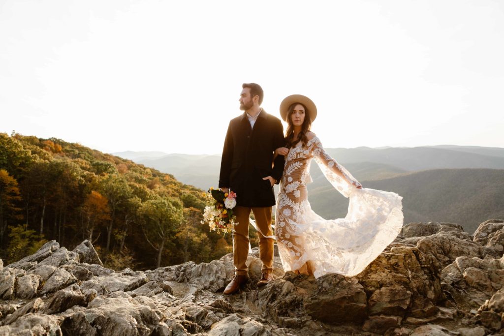 Bride holds onto groom's arm while swinging her bohemian dress out in the sun and the groom holds the floral bouquet. The wedding couple post for portraits after their ceremony during their Raven's Roost Overlook Elopement. 
