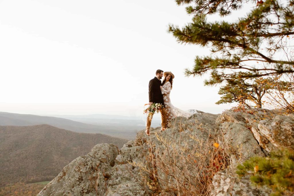 Bride and groom stand together on a cliff in the Virginia mountains at sunset during their Raven's Roost Overlook Elopement. 