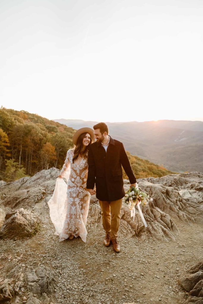Bride and groom walk together, smiling and holding hands during their sunset Raven's Roost Overlook Elopement in the Virginia mountains. 