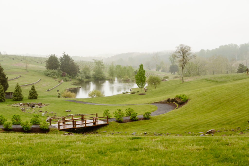 A rainy and foggy day at Stone Tower Winery, Leesburg Virginia. A bridge with a winding road is visible that leads to a lake.