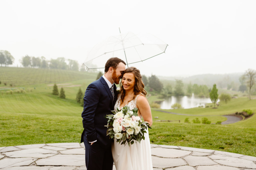 Wedding Couples snuggle under clear umbrella after their ceremony at Stone Tower Winery in Leesburg, Virginia