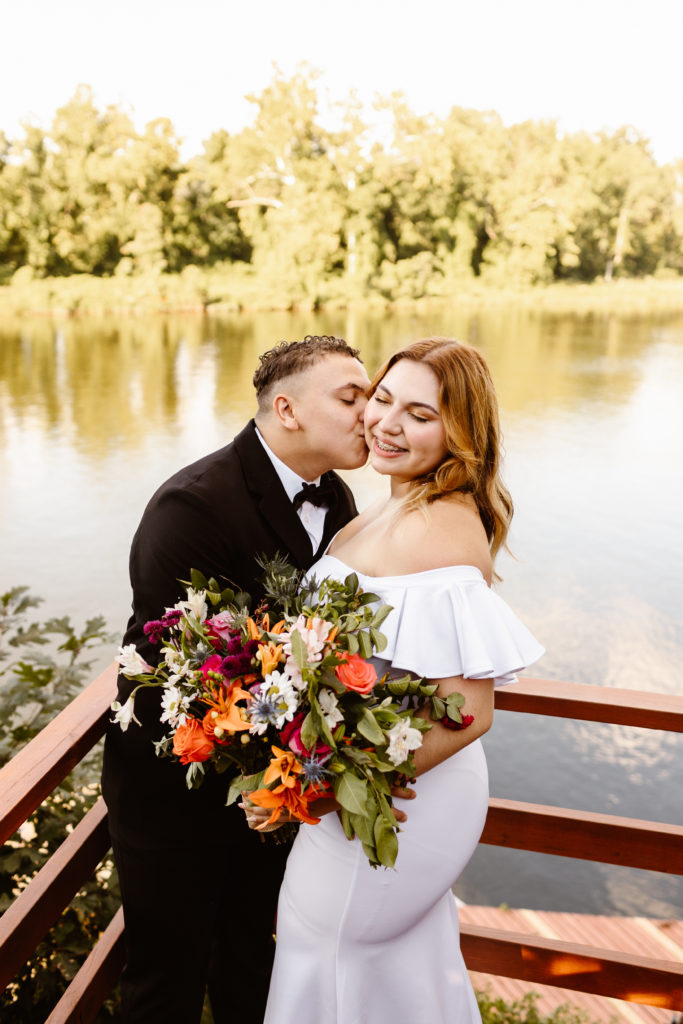 Groom kisses bride's cheek on dock overlooking the Occoquan river during their elopement. 