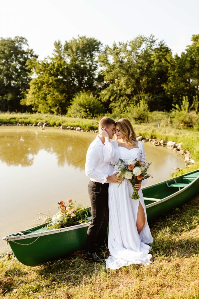 Wedding couple embrace each other at a lake next to a canoe during their Maryland elopement day. 