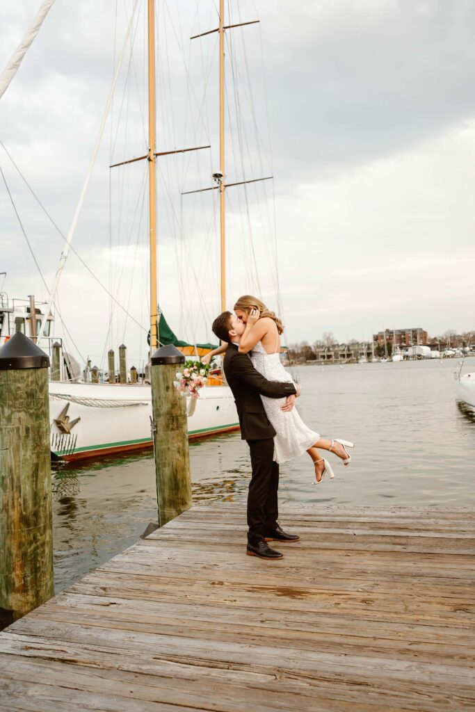 Groom holds bride up in the air while kissing her on the docks on downtown Annapolis during their Maryland elopement. 