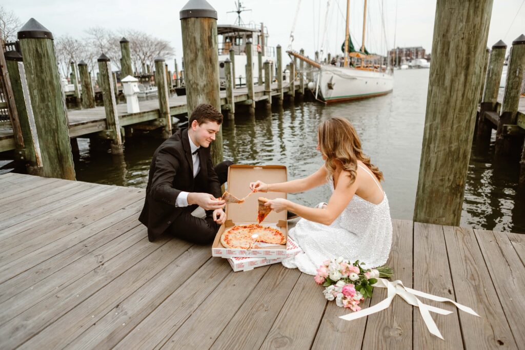 Wedding couple enjoy a pizza sitting on the docks of the downtown historic Annapolis waterfront on the elopement day in Maryland. 