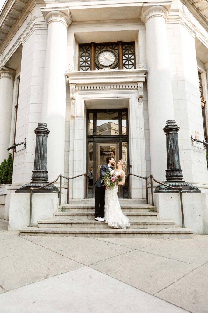 Wedding couple pose with flowers on the steps of the Citizen's Ballroom wedding venue in downtown Frederick, Maryland on their elopement day. 
