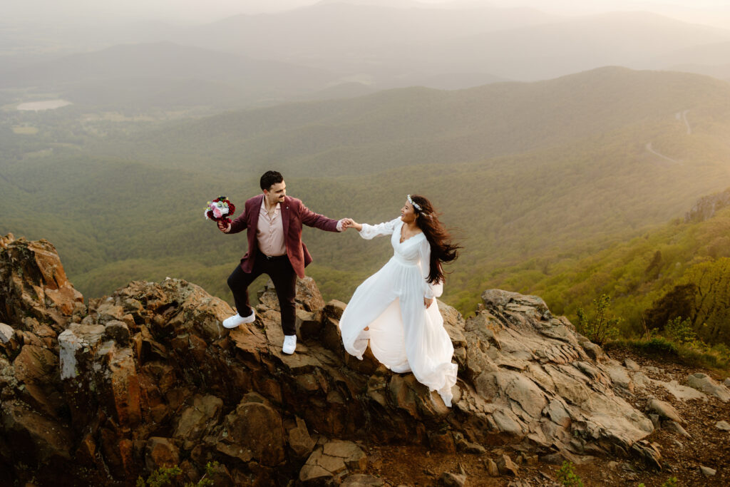 Bride and groom stand holding hands on rocks at sunrise at Stony Man Trail Summit in Shenandoah National Park during their Virginia elopement. 