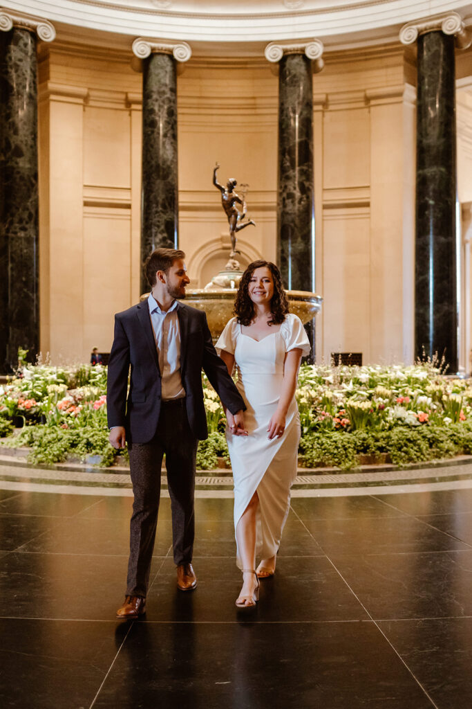 The couple dressed in wedding attire as they walk through the National Gallery of Art