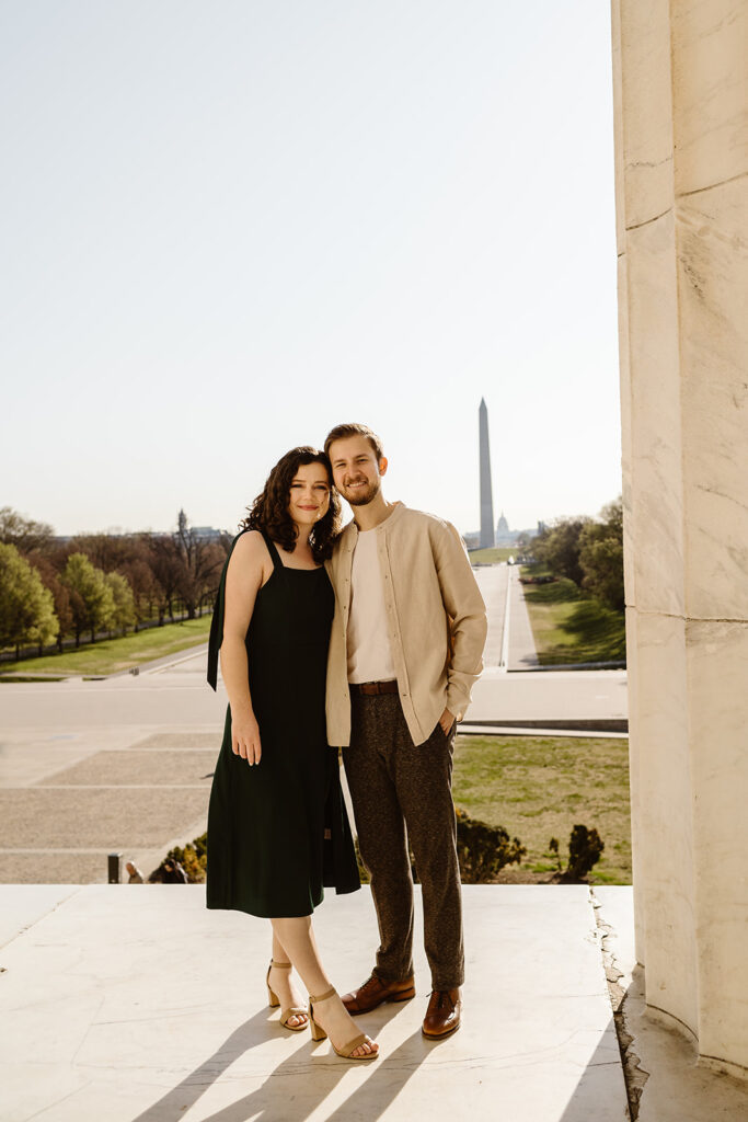 The engaged couple smiling at the camera at the Lincoln Memorial for classic engagement photos