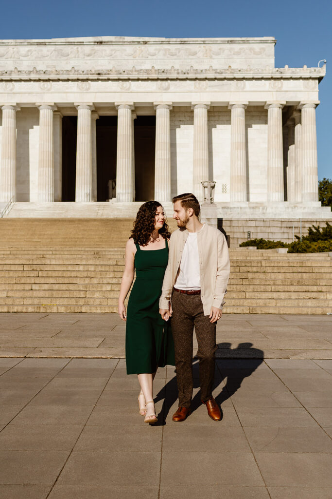 The engaged couple walking towards their DC wedding photographer during their DC engagement photos in front of the Lincoln Memorial.