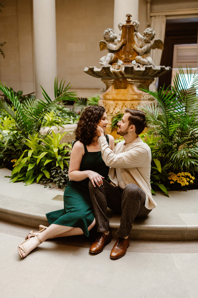 The couple sitting together by the foundation in the National Gallery of Art for romantic Washington DC engagement photos