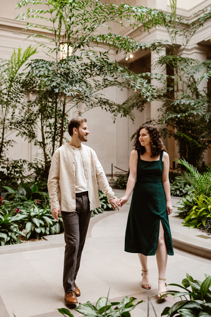 The engaged couple holding hands as they stroll through the gardens in the National Gallery of Art