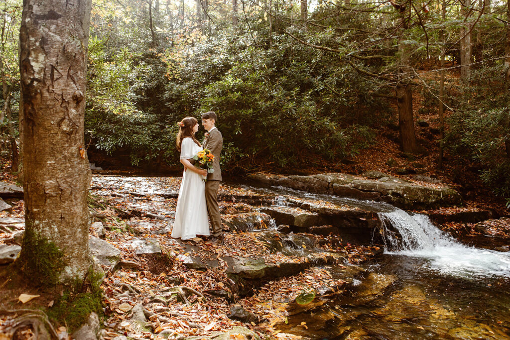 the wedding couple standing on top of the waterfall for elopement photos in the fall