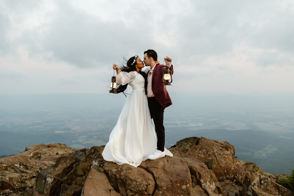 the wedding couple holding lanterns as they kiss on top of the cliffs