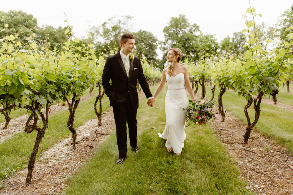 the wedding couple walking hand in hand through the vineyard