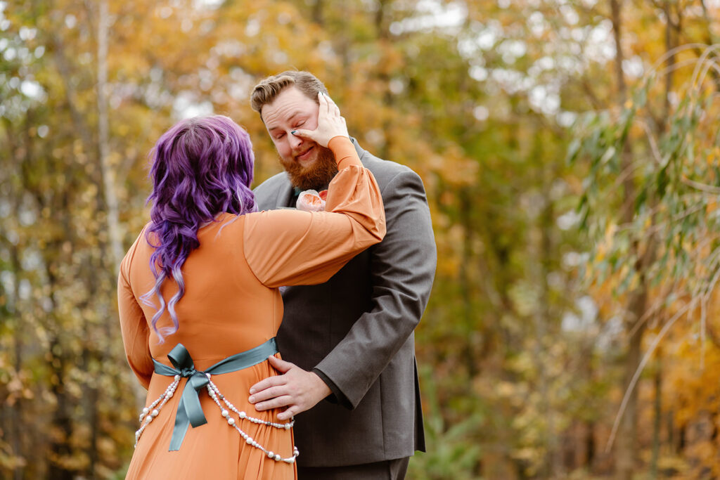 the bride wiping away tears from the groom during their first look at their fall elopement