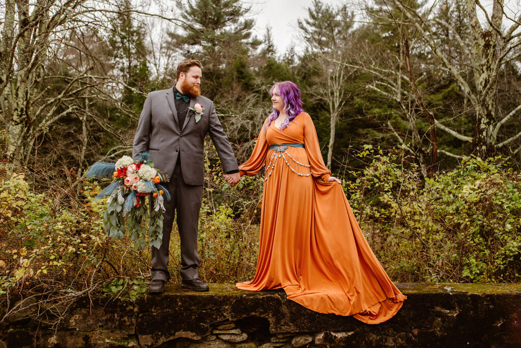 the bride and groom holding hands and standing on a log for their fall elopement photos