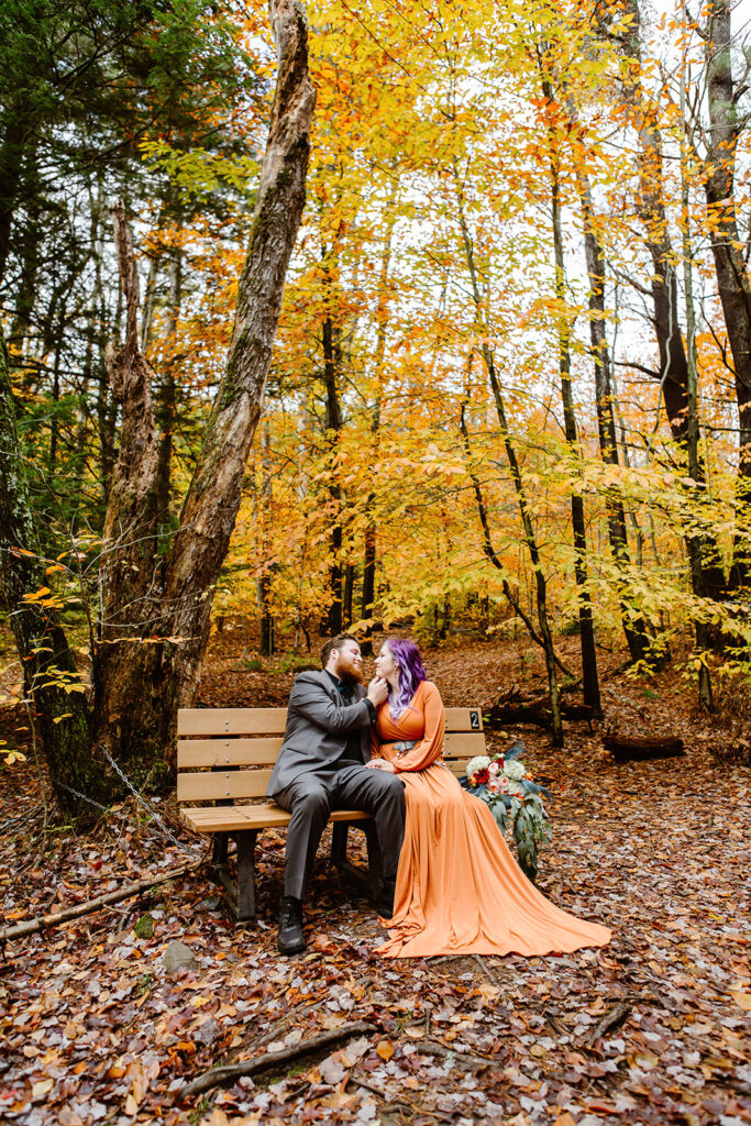 the wedding couple sitting on a bench during their fall elopement photos