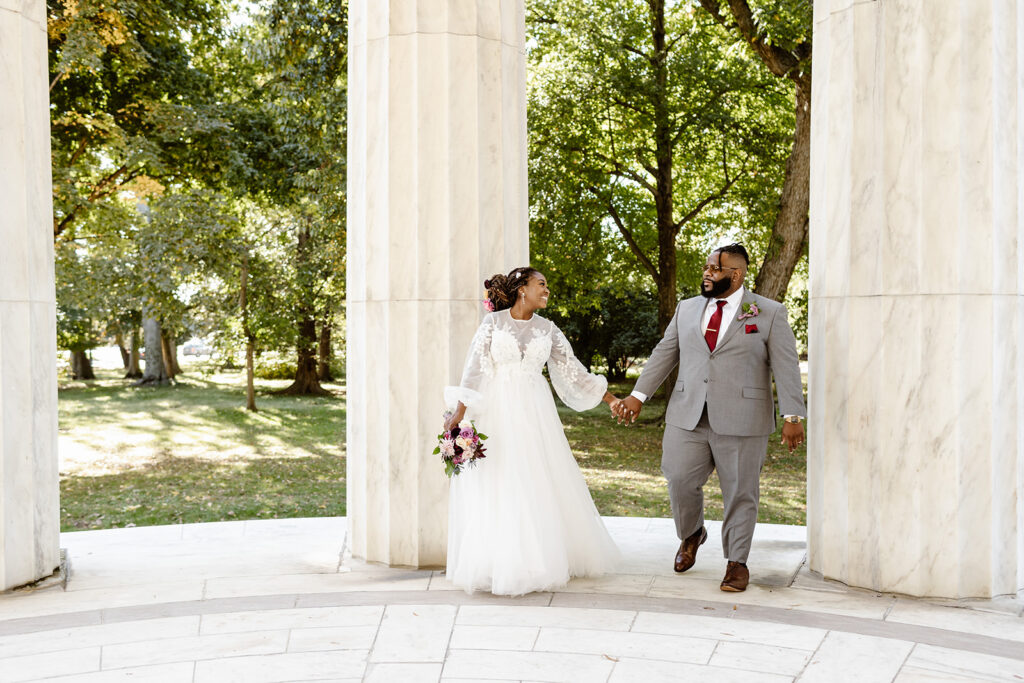 the wedding couple holding hands as they walk through the dc war memorial